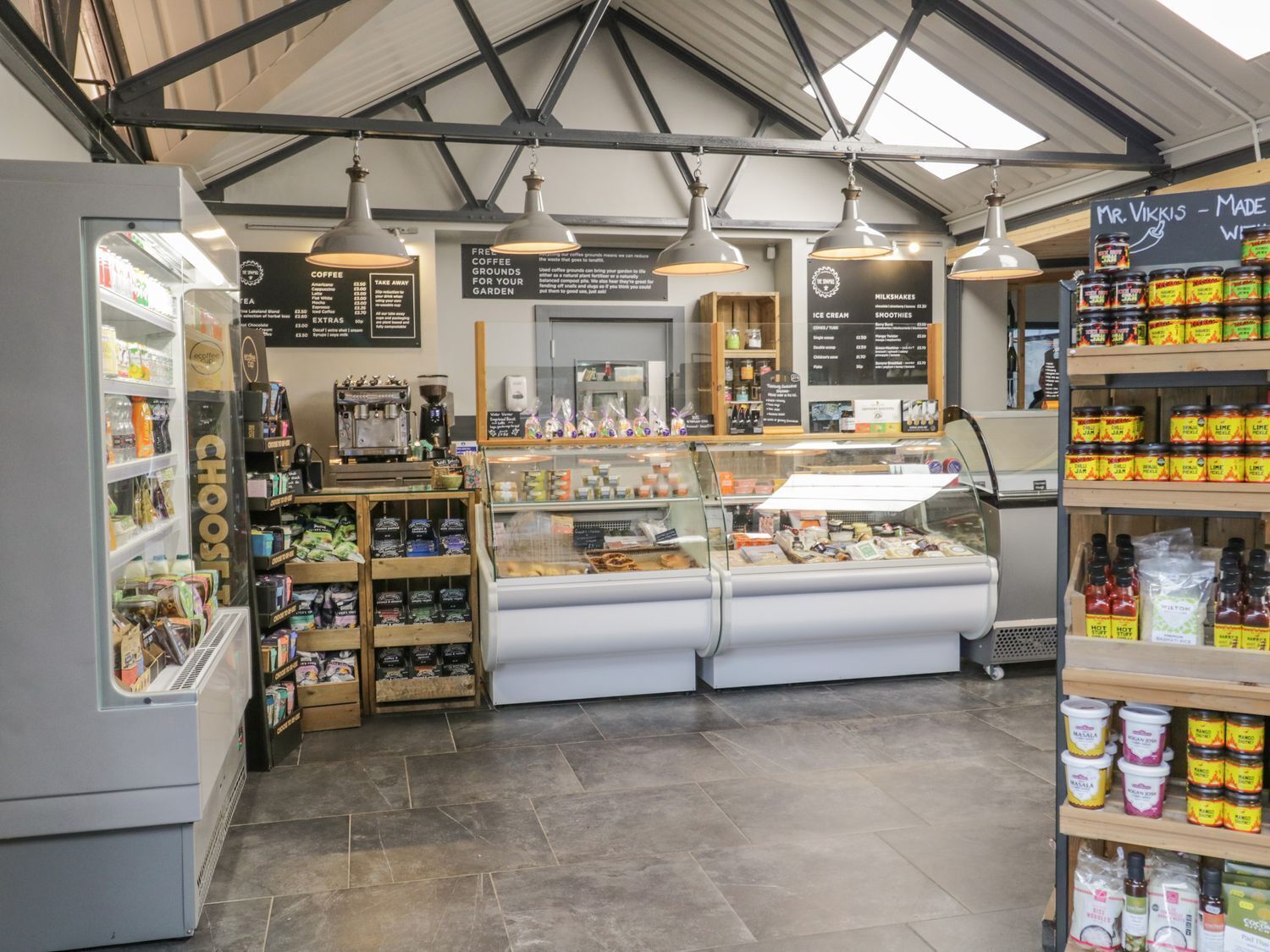 A cafe interior with a coffee machine, shelves with snacks, a seating area, and a display of ice cream and smoothies.