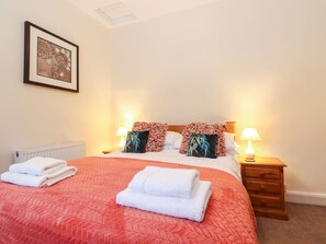 A neatly made bed with a red quilt, two pillows with floral patterns, and two bedside lamps. - Irt Cottage (Seascale)
