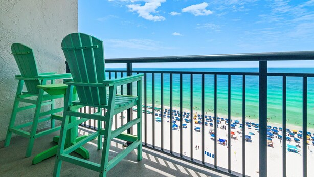A balcony with two green Adirondack chairs overlooking a beach with umbrellas and people. - Sundestin 1409 (Destin)