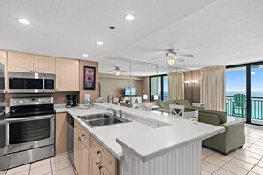 A modern kitchen with stainless steel appliances, a large island with a sink, and a dining area with a view of the ocean. - Sundestin 1409 (Destin)