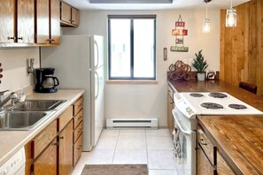 Una cocina con armarios de madera, un refrigerador, una estufa, una cafetera y un ventanal.