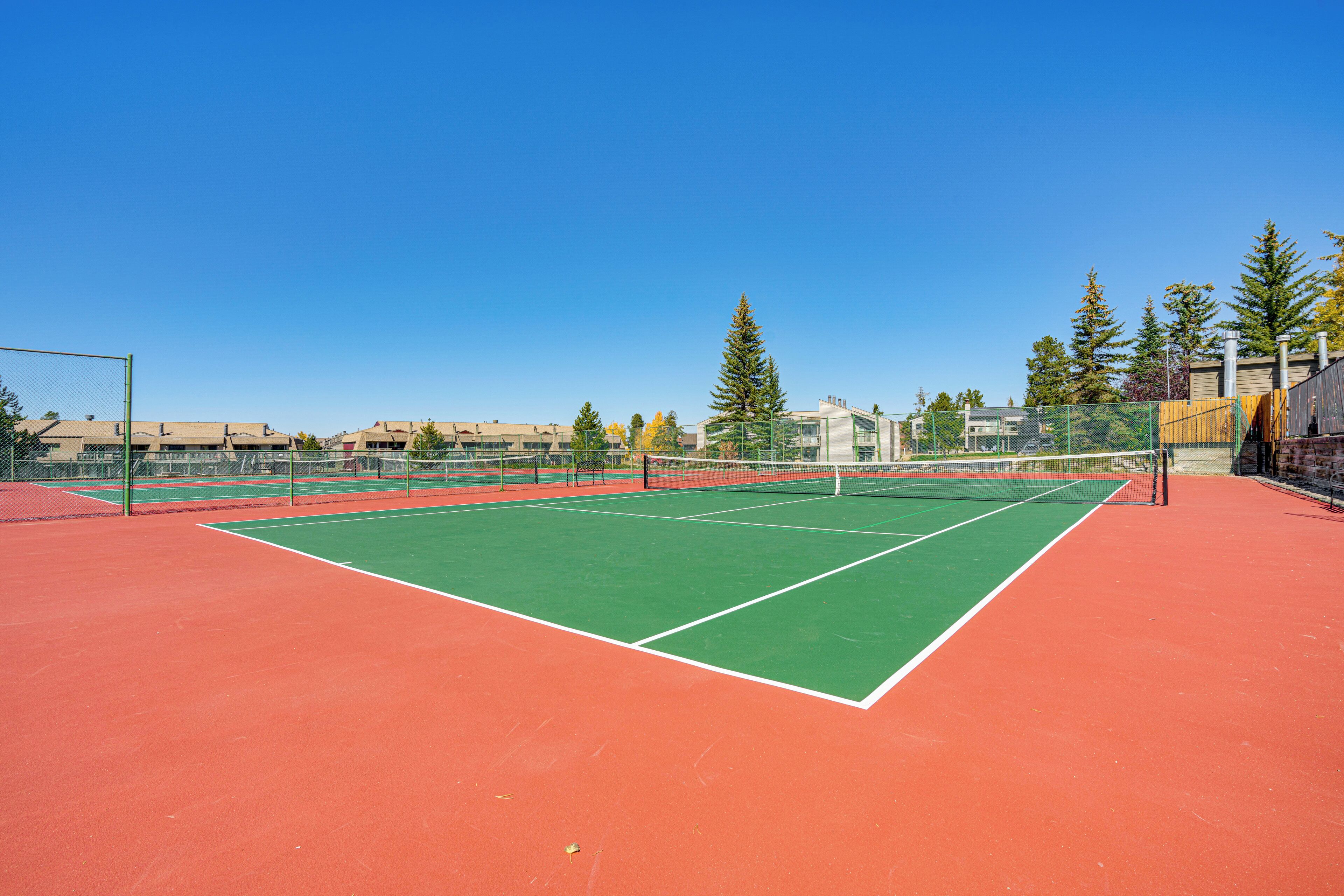 A tennis court with a net, surrounded by a fence and trees.