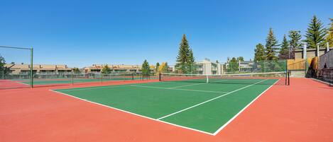 A tennis court with a net, surrounded by a fence and trees.
