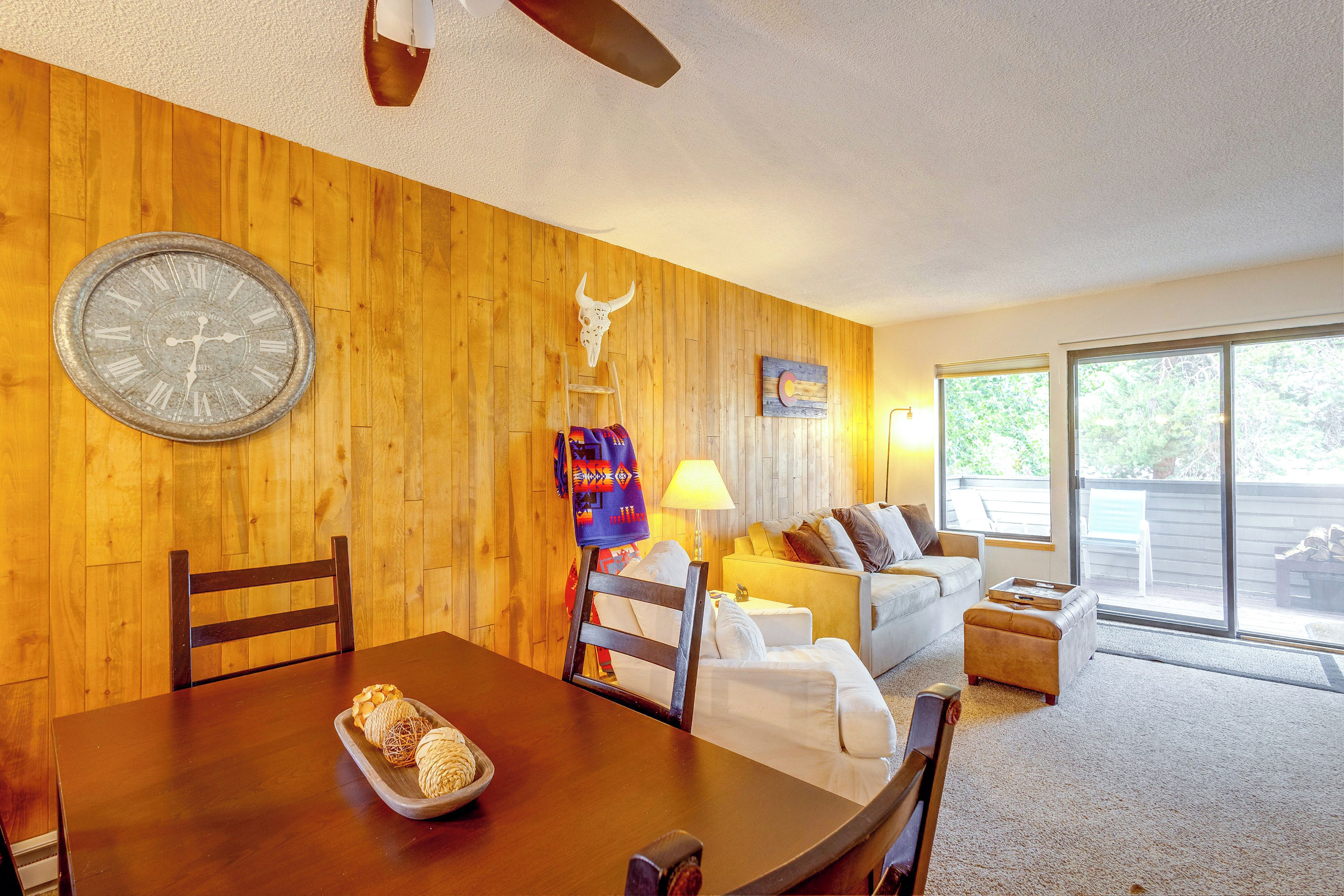 A wooden-paneled room with a dining table, chairs, a sofa, and a large wall clock.