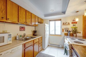 A kitchen with wooden cabinets, a refrigerator, a coffee maker, and a stove. - Fraser Condo w/ Pool & Hot Tubs: Close to Trails! (Fraser)
