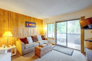 Sala de estar con una pared de madera, un sofá, un televisor y vistas al exterior.