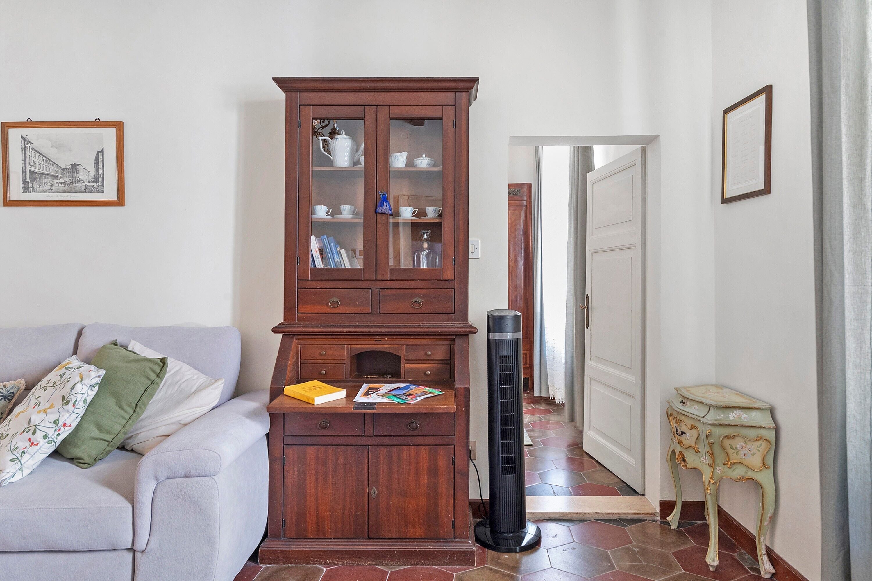 Un salon comprenant un canapé, un meuble en bois avec des portes en verre, un radiateur noir et un petit guéridon sur lequel est posé un objet décoratif.