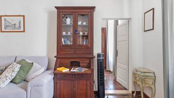Un salon comprenant un canapé, un meuble en bois avec des portes en verre, un radiateur noir et un petit guéridon sur lequel est posé un objet décoratif.
