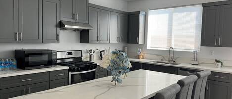 A modern kitchen with grey cabinets, a white marble island, and a stainless steel range hood.