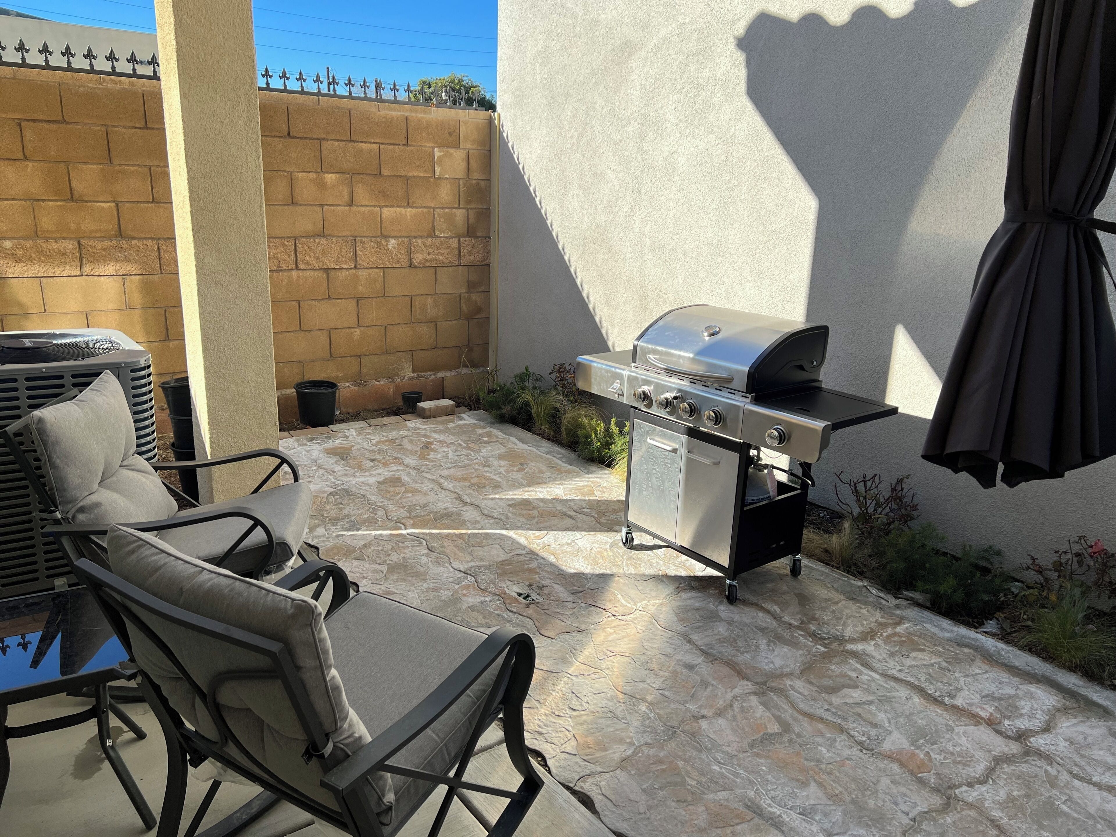 An outdoor patio with a barbecue grill, seating area, and a brick wall.