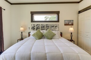 Uma cama bem arrumada com um edredom branco, duas almofadas verdes e uma janela acima.
