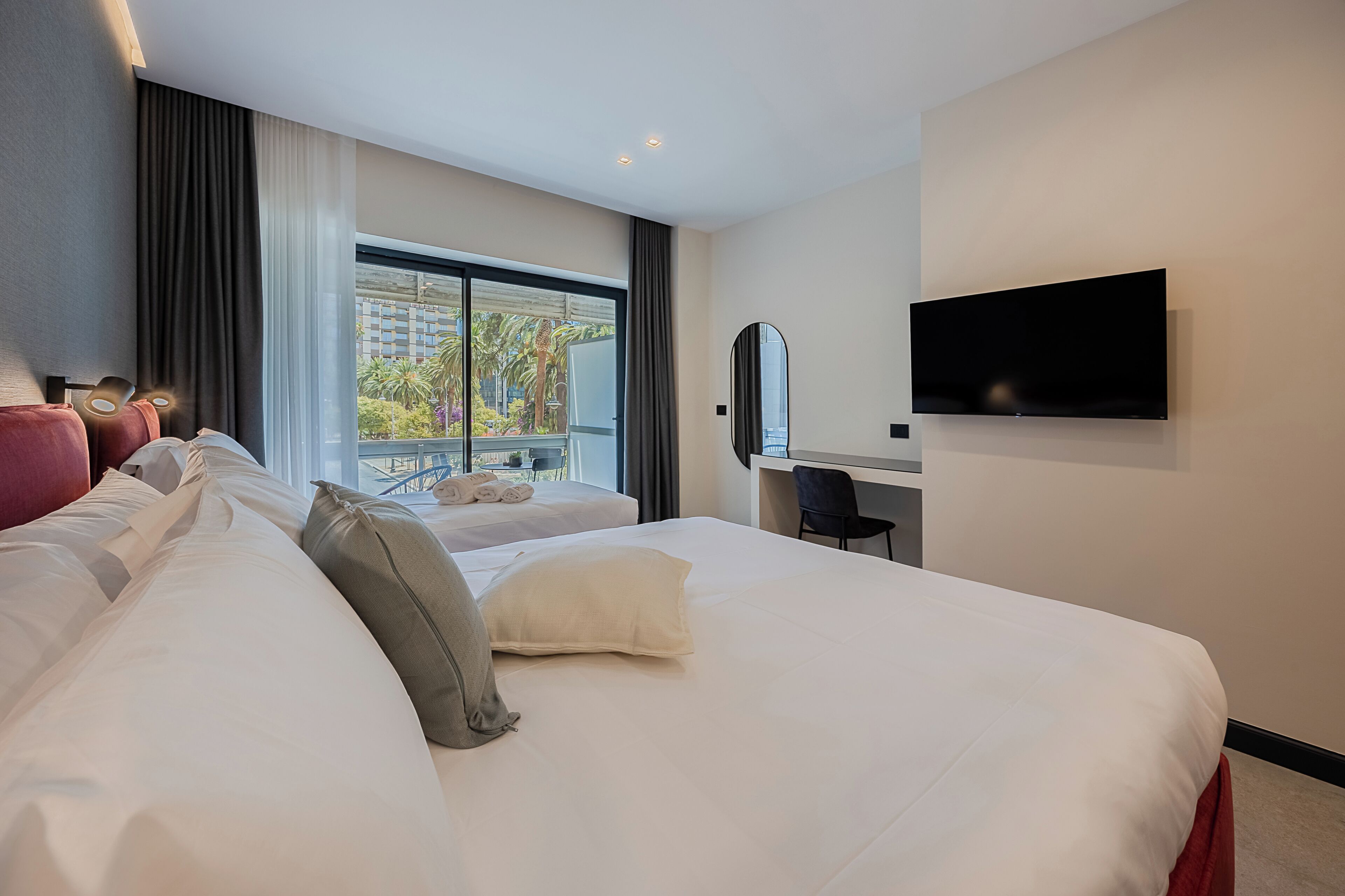 A hotel room with a large bed, a desk, a flat-screen TV, and a view of the city through the window.