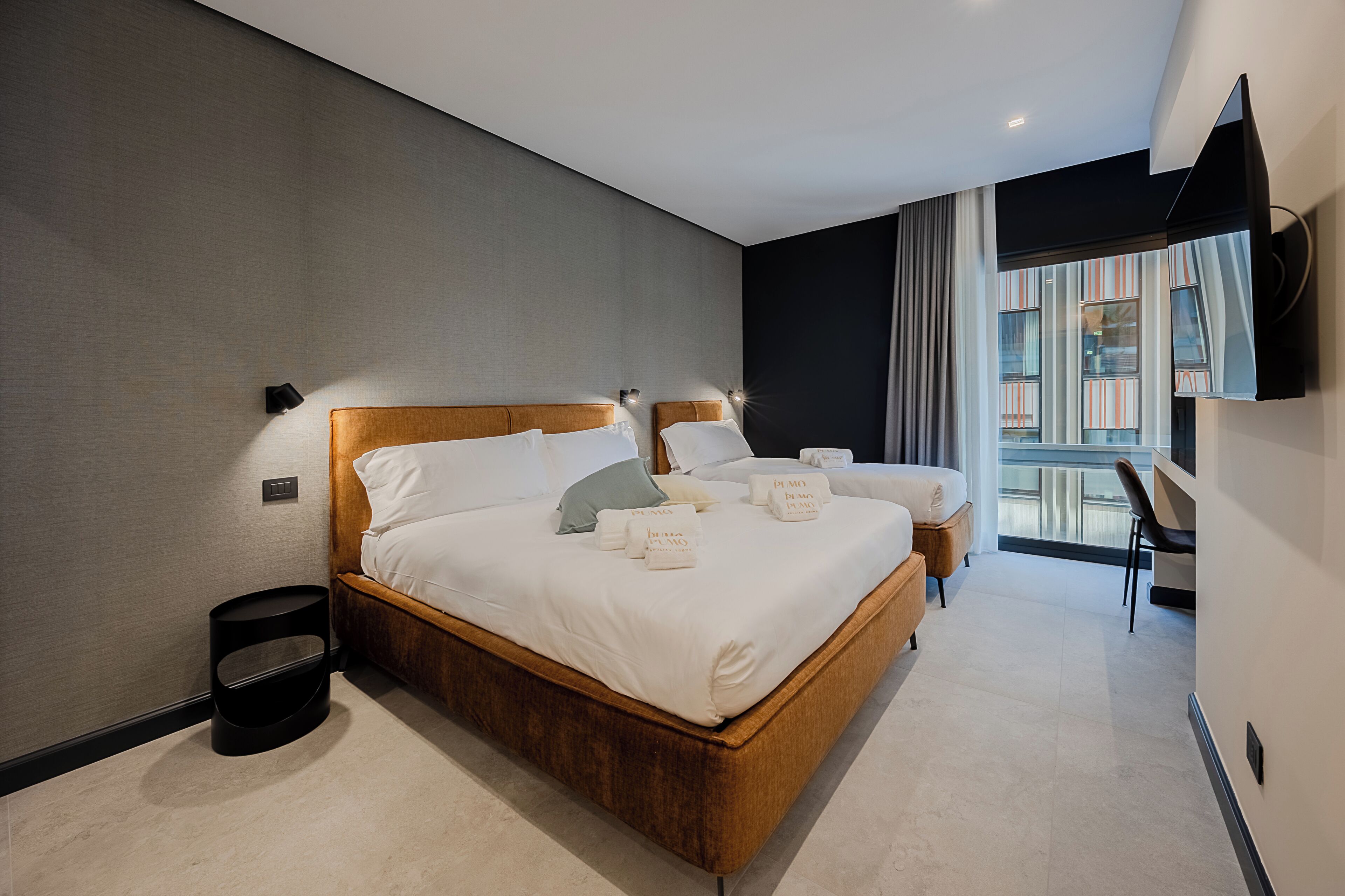 Una habitación de hotel moderna con una cama grande, mesitas de noche, una silla y un televisor montado en la pared.