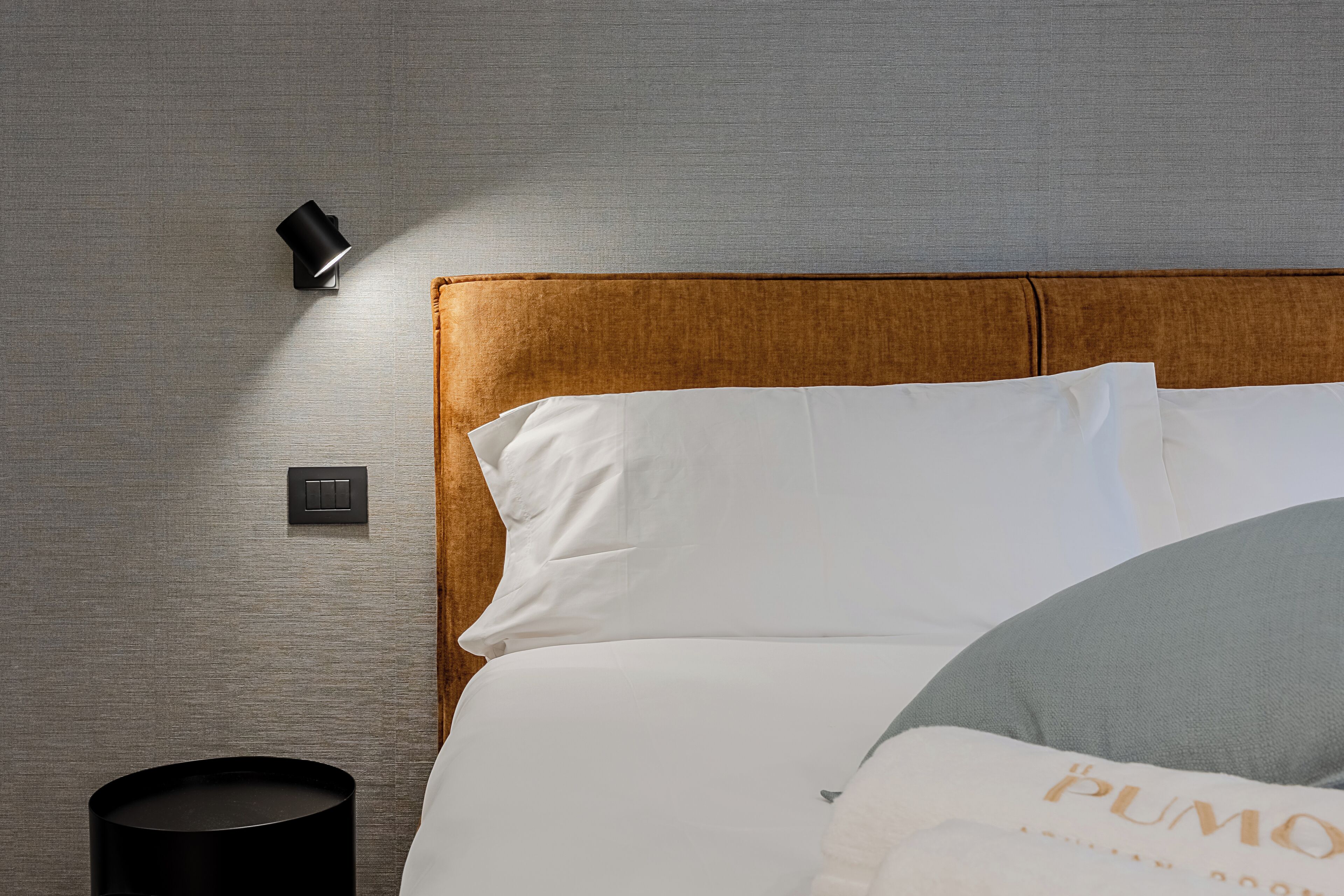 A hotel room with a bed, a nightstand, a lamp, and a wall switch.