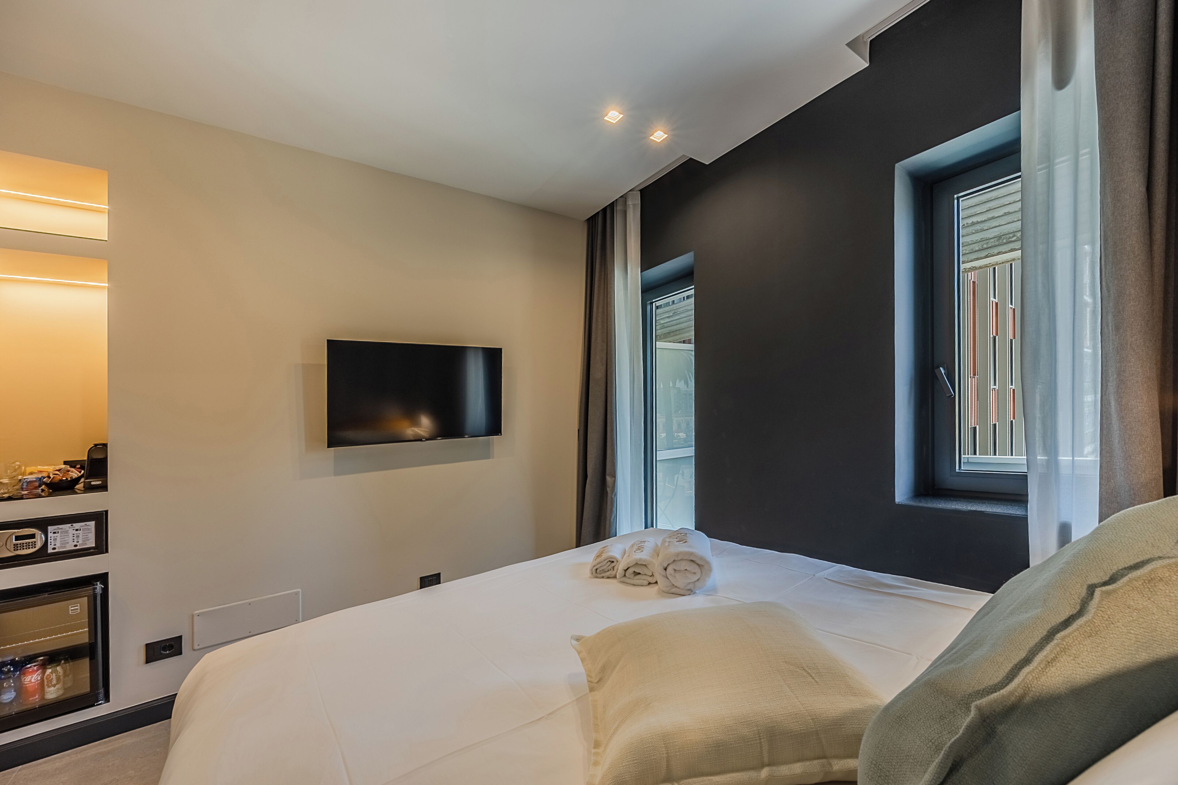 Ein modernes Hotelzimmer mit einem großen Bett, einem flachbildfernseher an der Wand und einem Fenster mit Vorhängen.