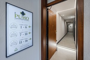 Un couloir d’hôtel avec un panneau indiquant les numéros des chambres et un numéro de téléphone à contacter en cas de besoin.