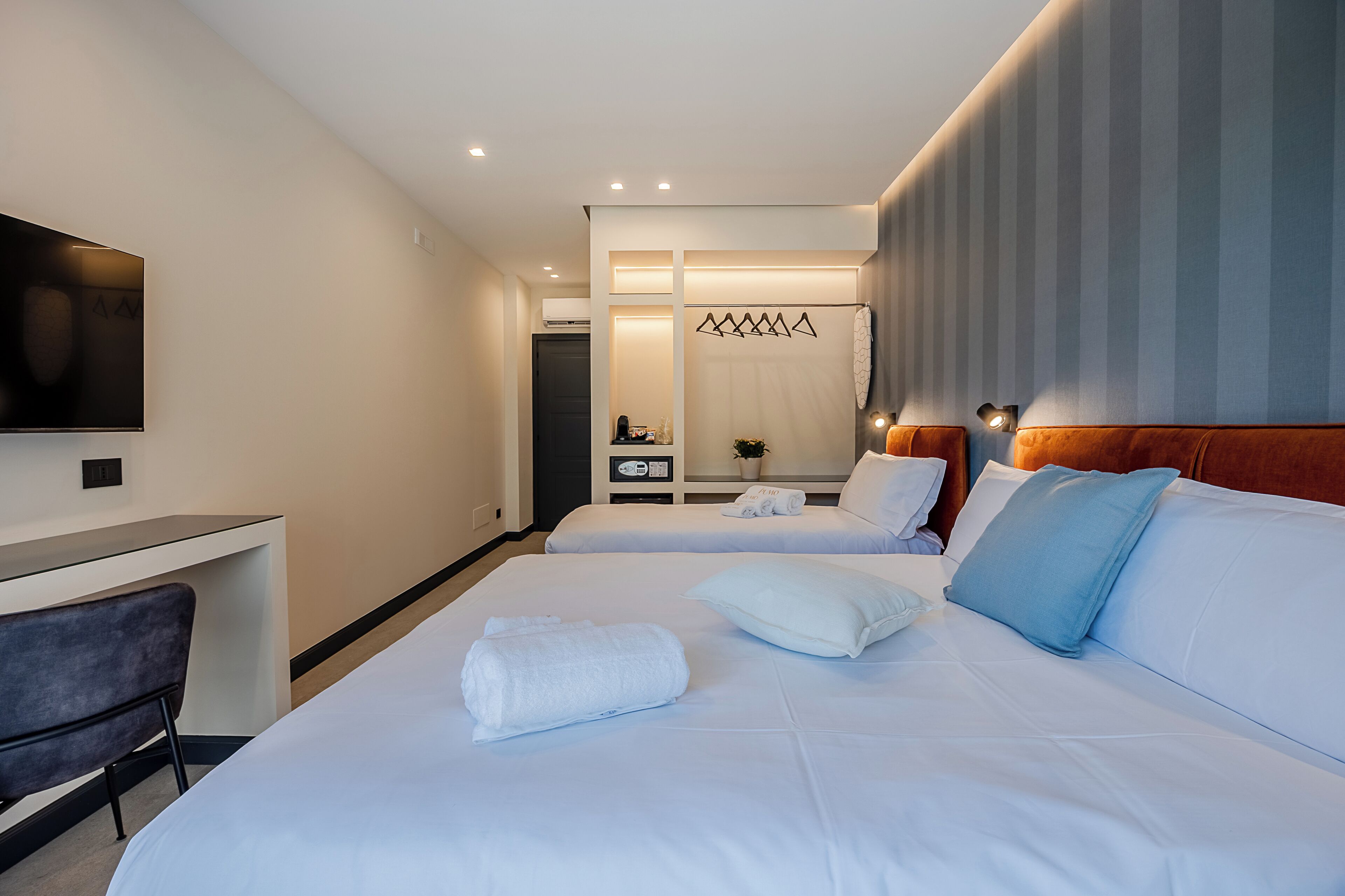 A hotel room with two beds, a desk, a television, and a shower area.