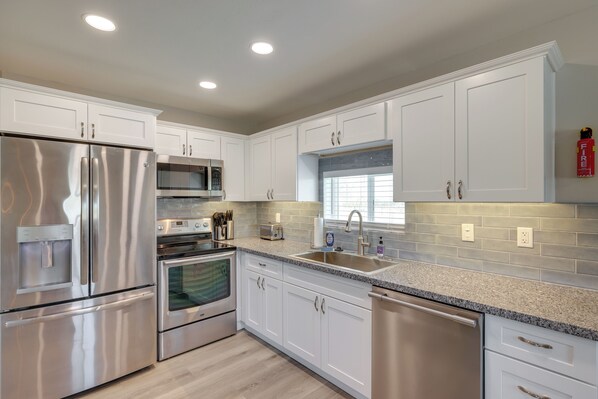 A modern kitchen with stainless steel appliances, white cabinetry, and a granite countertop.