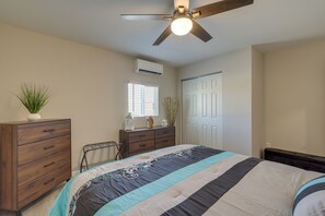 Un dormitorio con cama, cómoda, ventilador de techo, ventana y aire acondicionado.
