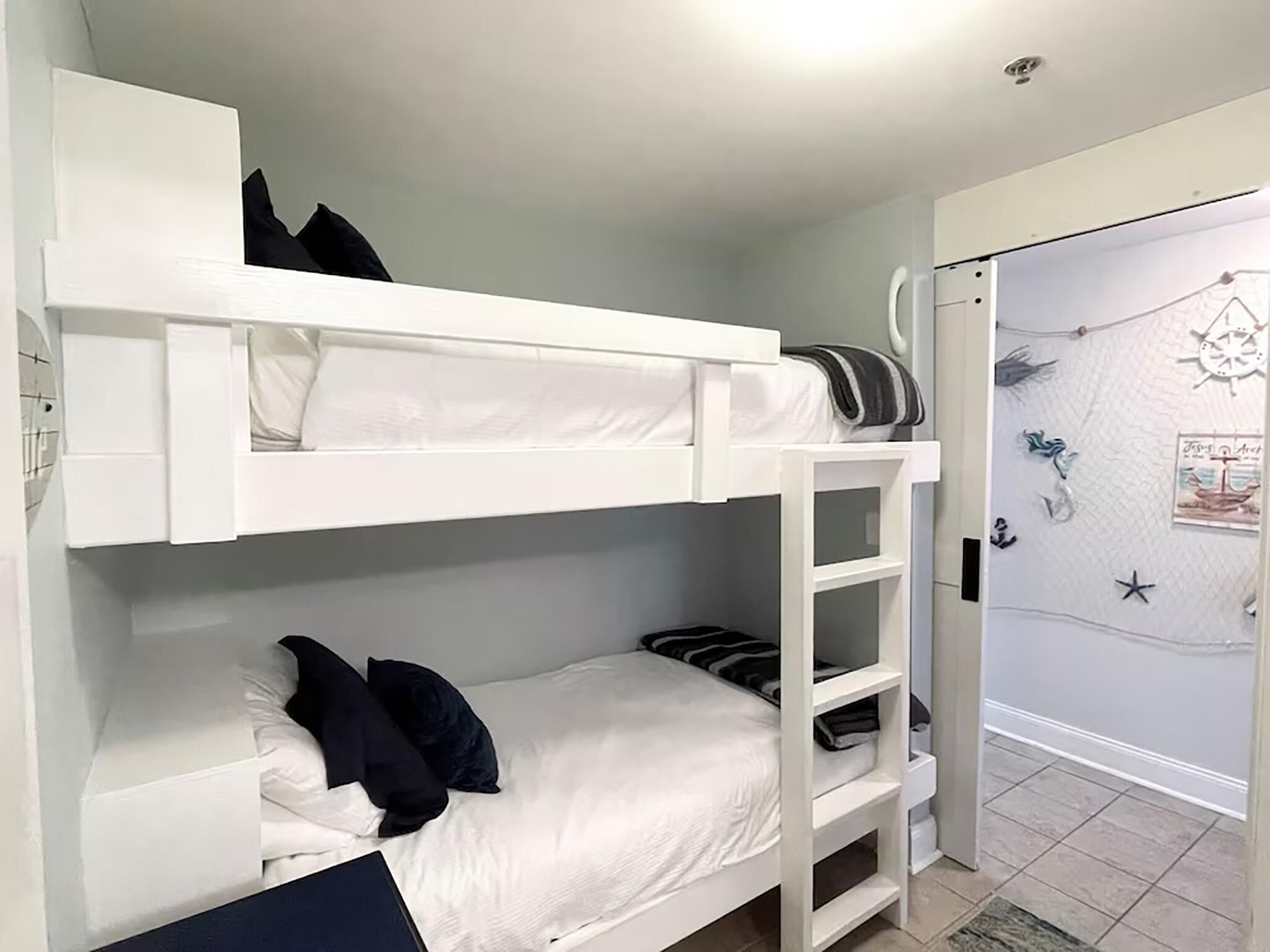 Habitación con literas, decoración en blanco, una puerta con adorno de estrella y un pequeño estante.