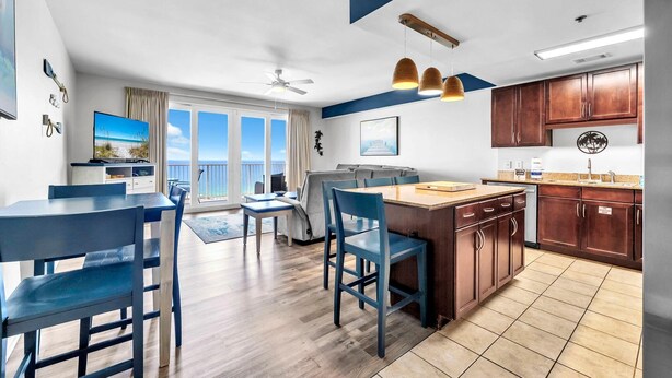 Een moderne keuken met houten kasten, een eethoek met blauwe stoelen en een groot raam met uitzicht op de oceaan.