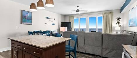 Cocina moderna con una isla central, comedor con sillas, un sofá y un ventanal con vistas.