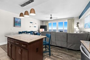 A modern kitchen with a central island, dining area with chairs, a sofa, and a large window with a view. - Laketown Wharf 1817 (Panama City Beach)