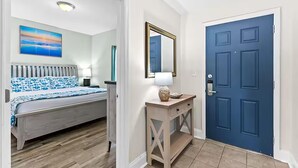 Een slaapkamer met een bed, nachtkastje, lamp en een schilderij aan de muur.