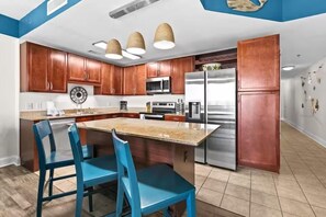 A modern kitchen with wooden cabinets, a stainless steel refrigerator, and a granite countertop. - Laketown Wharf 1817 (Panama City Beach)