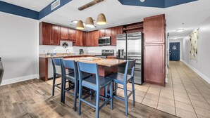 Een moderne keuken met houten kastjes, roestvrijstalen apparatuur en een centraal kookeiland met stoelen.