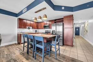 A modern kitchen with wooden cabinets, stainless steel appliances, and a central island with chairs. - Laketown Wharf 1817 (Panama City Beach)