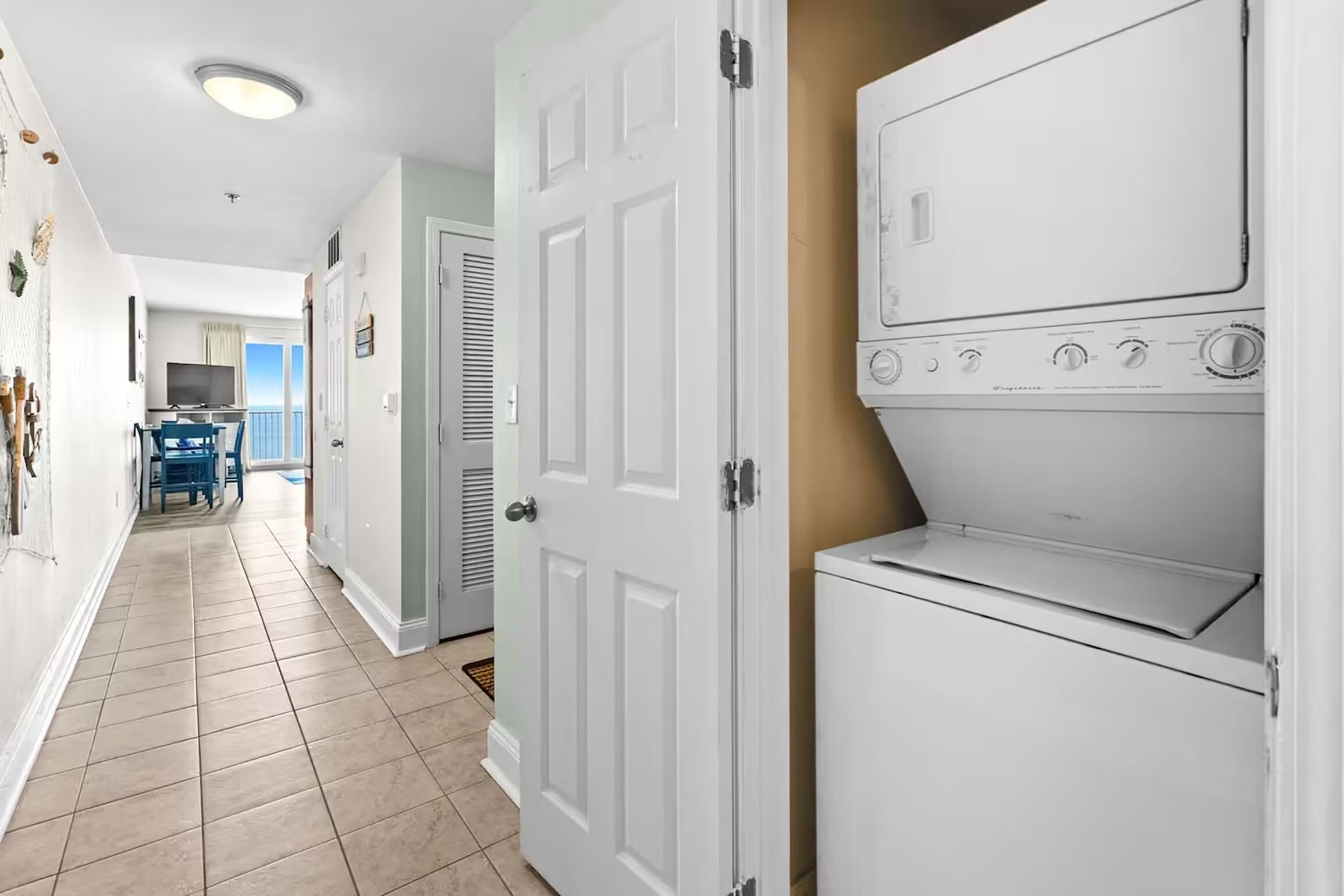 A laundry room with stacked washers and dryers, a tiled floor, and a hallway leading to a dining area. - Laketown Wharf 1817 (Panama City Beach)