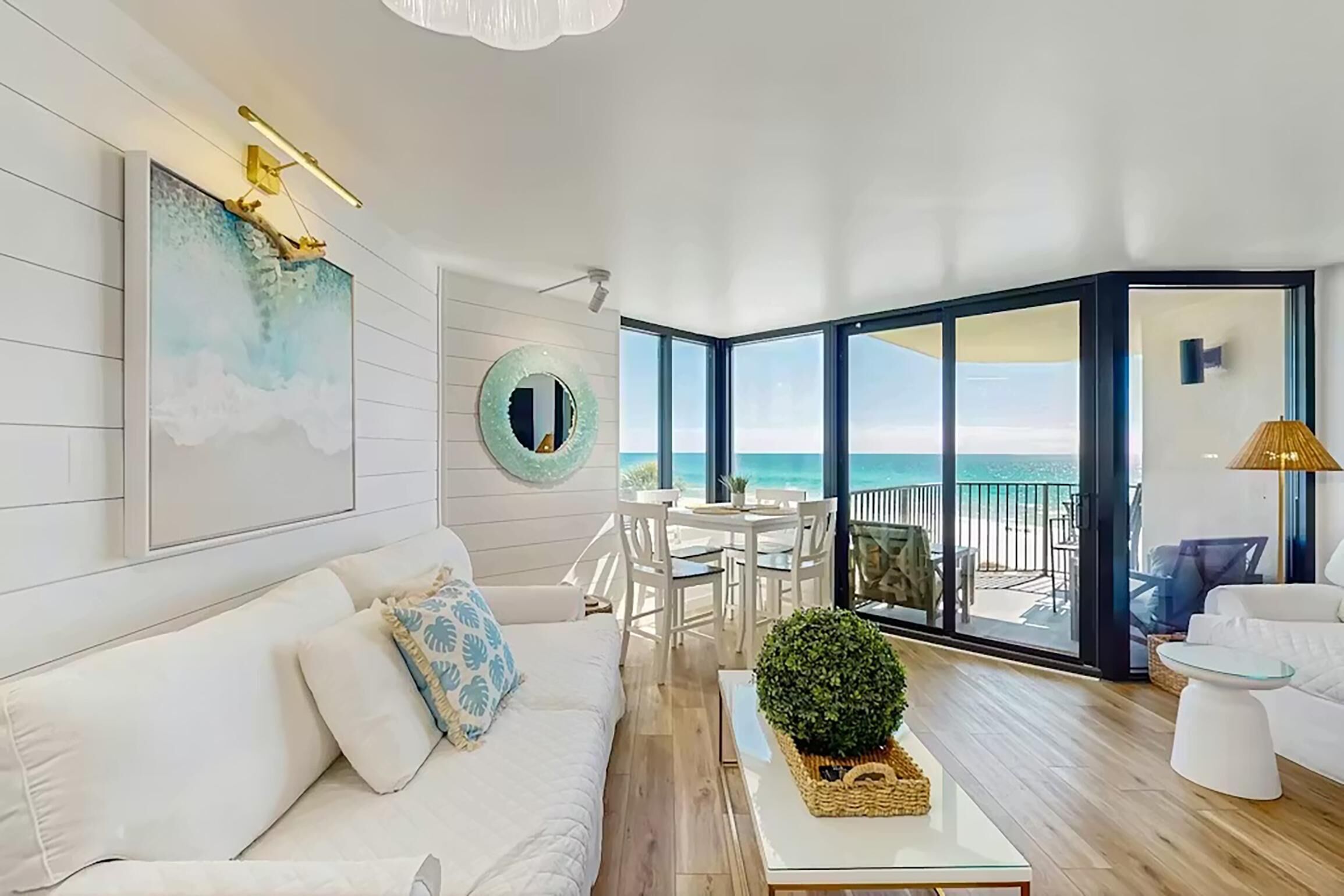 A modern living room with a white sofa, a round mirror, and a view of the ocean through large glass doors.