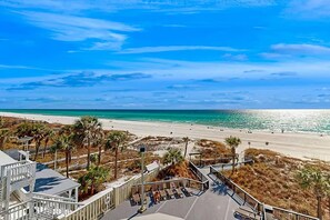 A beachfront property with a boardwalk leading to a pool area, overlooking a sandy beach and the ocean.