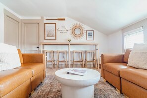 Ein gemütliches Wohnzimmer mit zwei Ledersofas, einem weißen Couchtisch und einem Essbereich mit Holztischen und Stühlen.