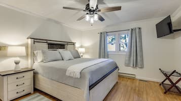 A bedroom with a bed, nightstands, a ceiling fan, a window with curtains, and a flat-screen TV mounted on the wall.