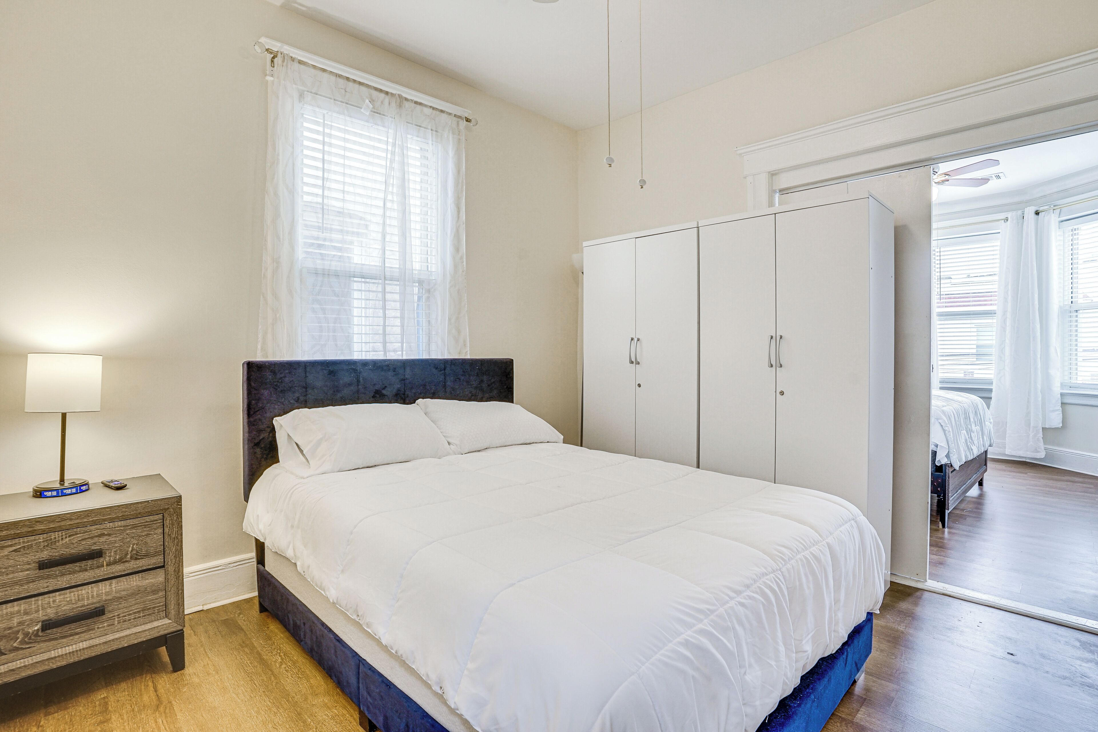 Un dormitorio con cama, armario, mesita de noche y ventana con cortinas.