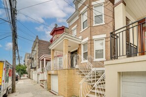 A residential street with brick houses, a visible garage door, and a parked delivery truck. - Near NYC Transit! Modern Gateway Region Apt (West New York)
