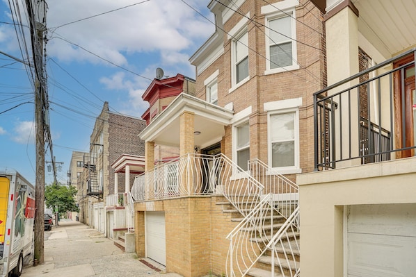 A residential street with brick houses, a visible garage door, and a parked delivery truck. - Near NYC Transit! Modern Gateway Region Apt (West New York)