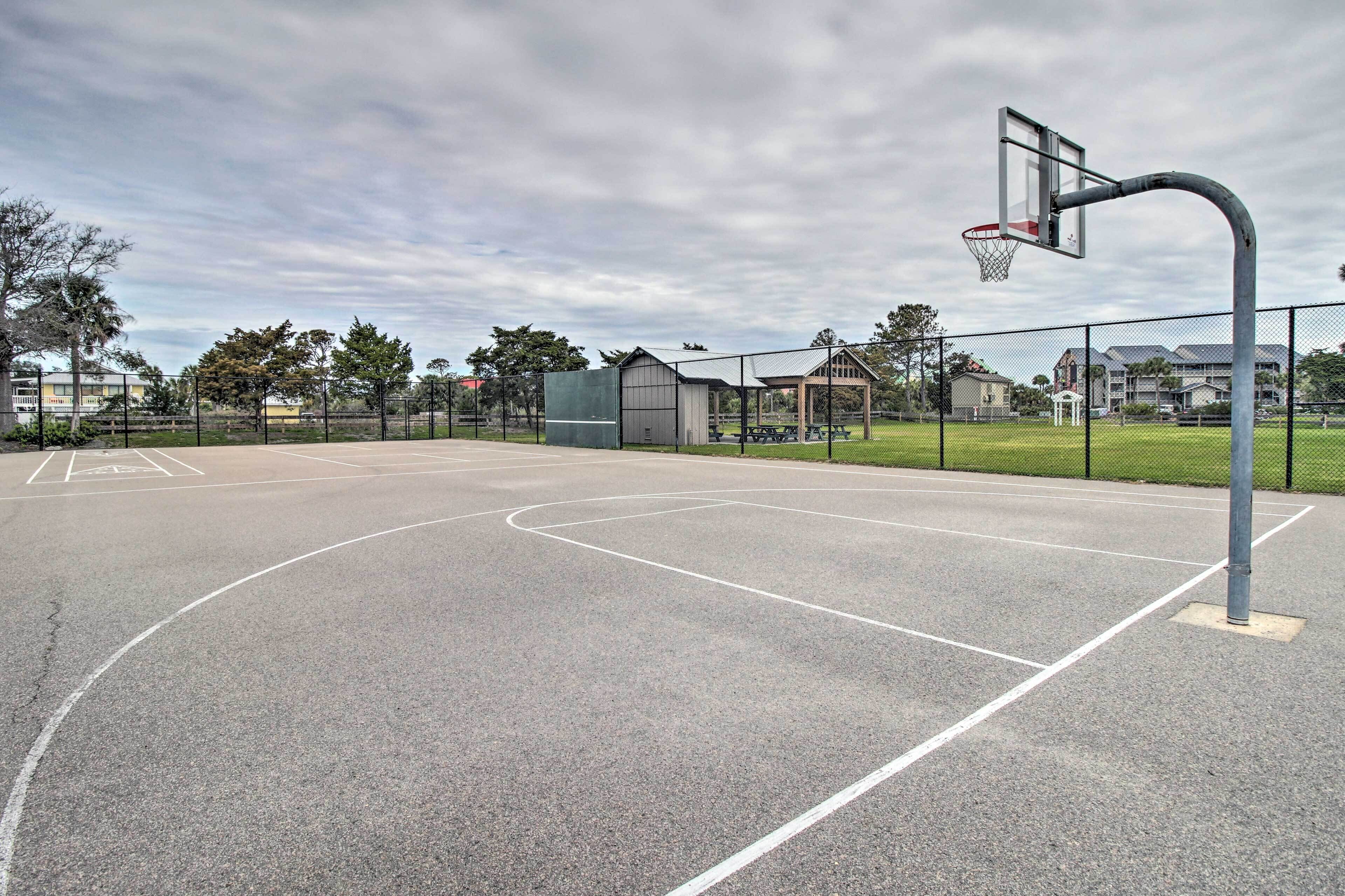An outdoor basketball court with a hoop, benches, and a fence.