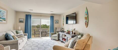 A spacious living room with a large window, a flat-screen TV, and a dining area with a table and chairs.