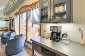 A modern kitchen with a built-in coffee maker, a wooden cabinet with glass doors, and a seating area with chairs.