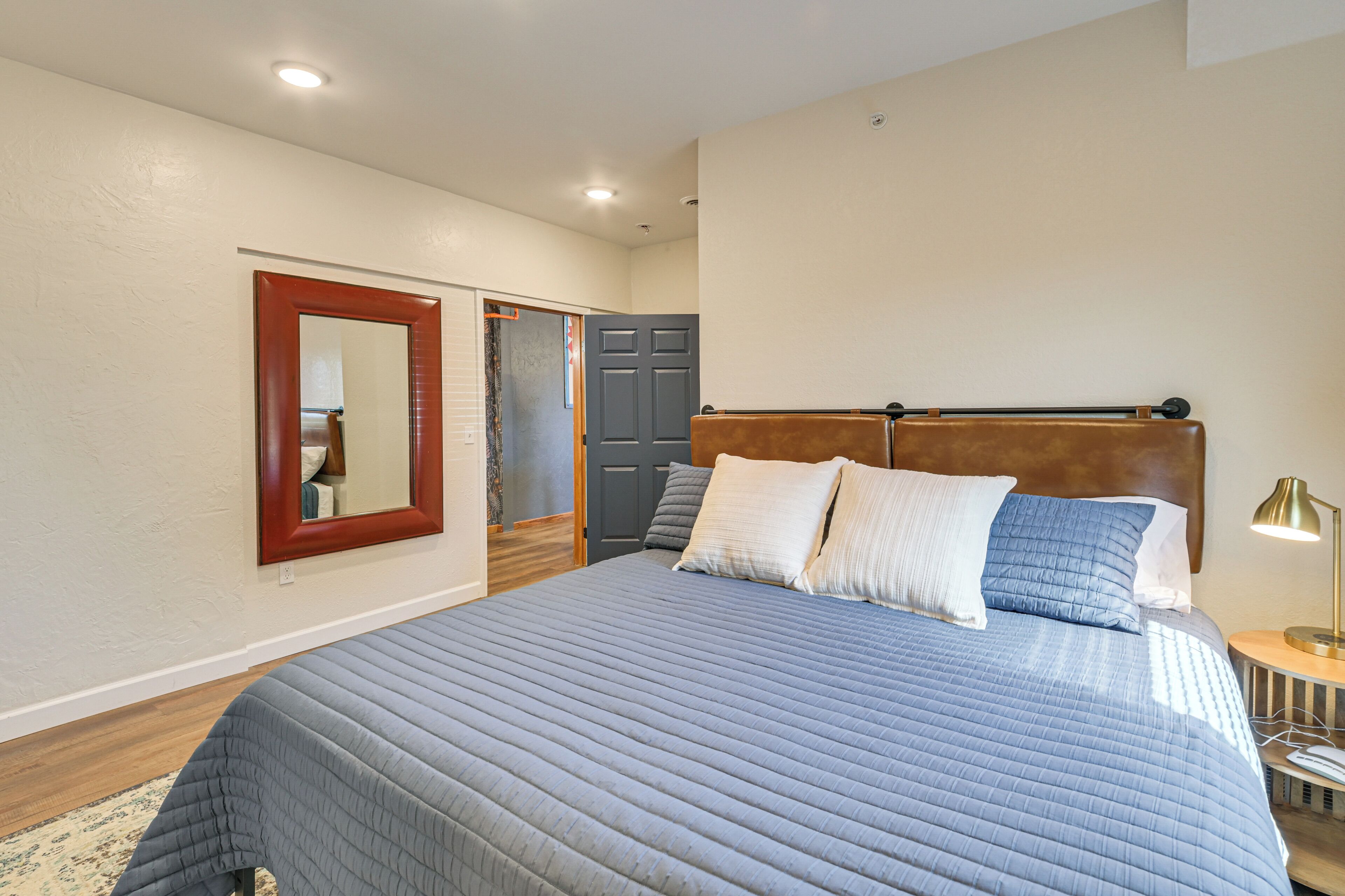 A bedroom with a large bed, a nightstand, a lamp, a mirror, and a wardrobe.
