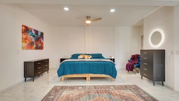 Un dormitorio con cama, cómoda, silla, alfombra, ventilador de techo y un cuadro.