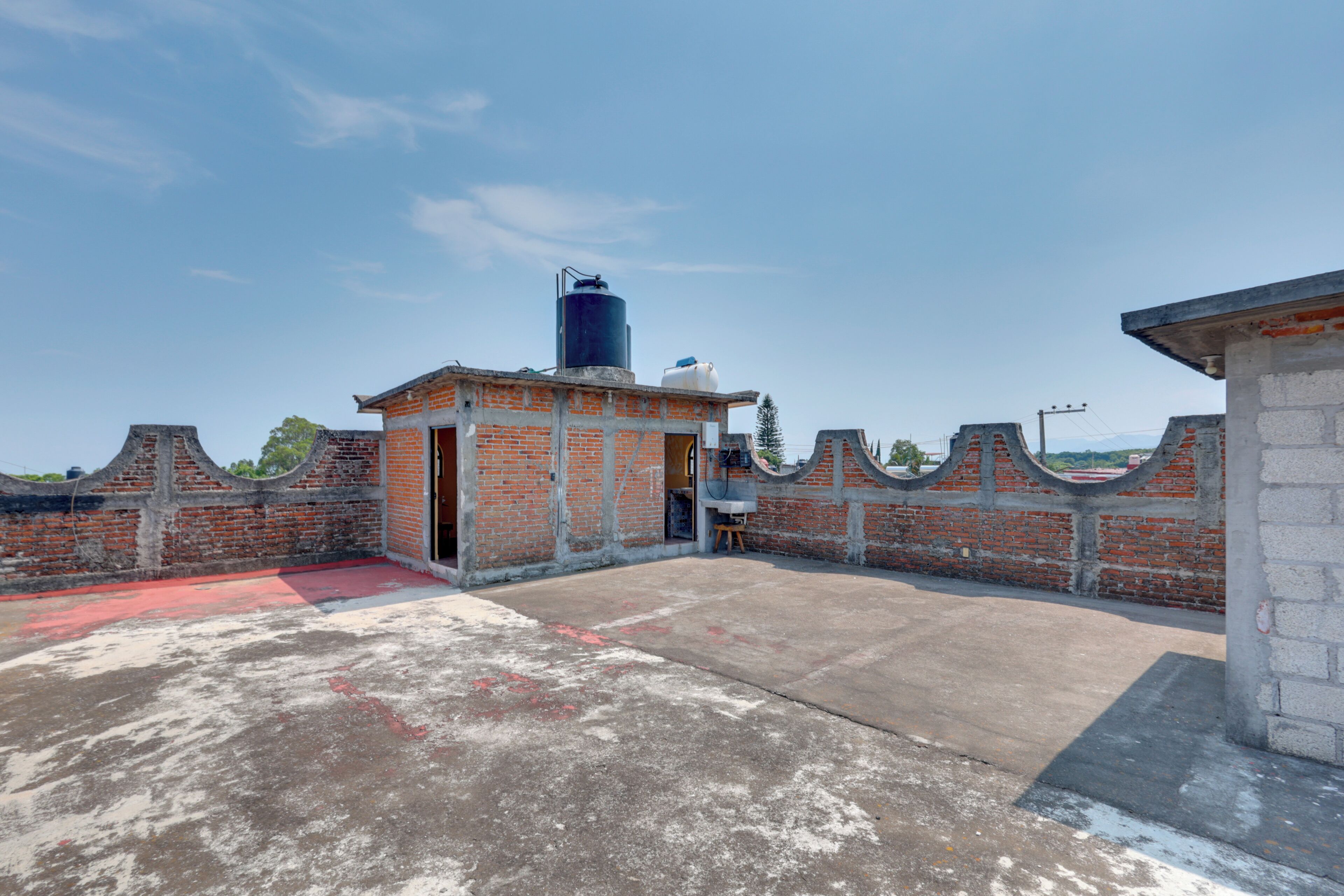 Una azotea con un muro de ladrillo, un edificio pequeño y un depósito de agua grande.
