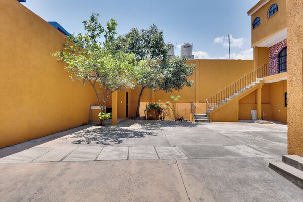 A courtyard with a staircase leading to a second floor, surrounded by yellow walls and a tree providing shade.