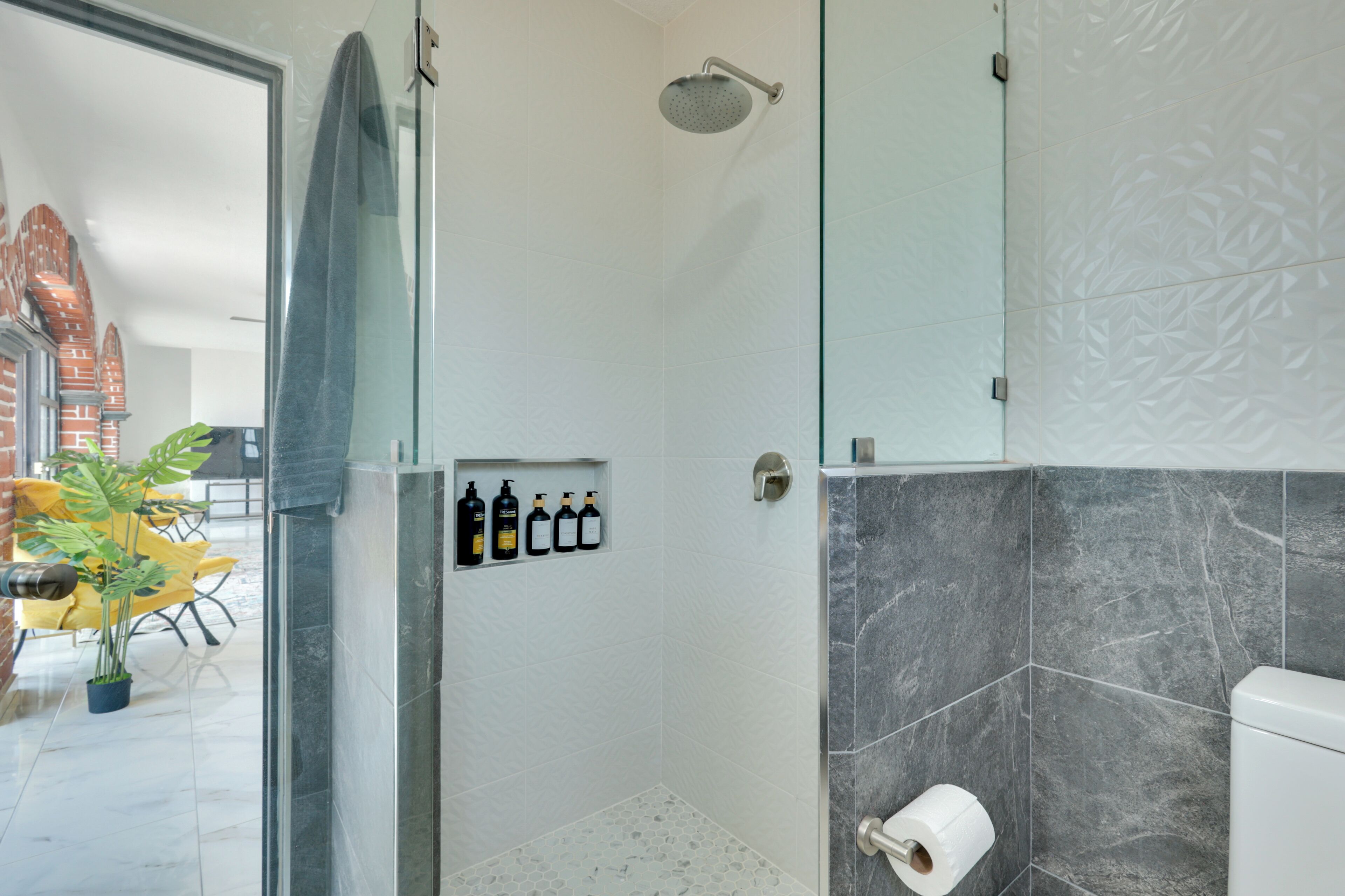 A modern bathroom with a shower, toilet, and a shelf with toiletries.