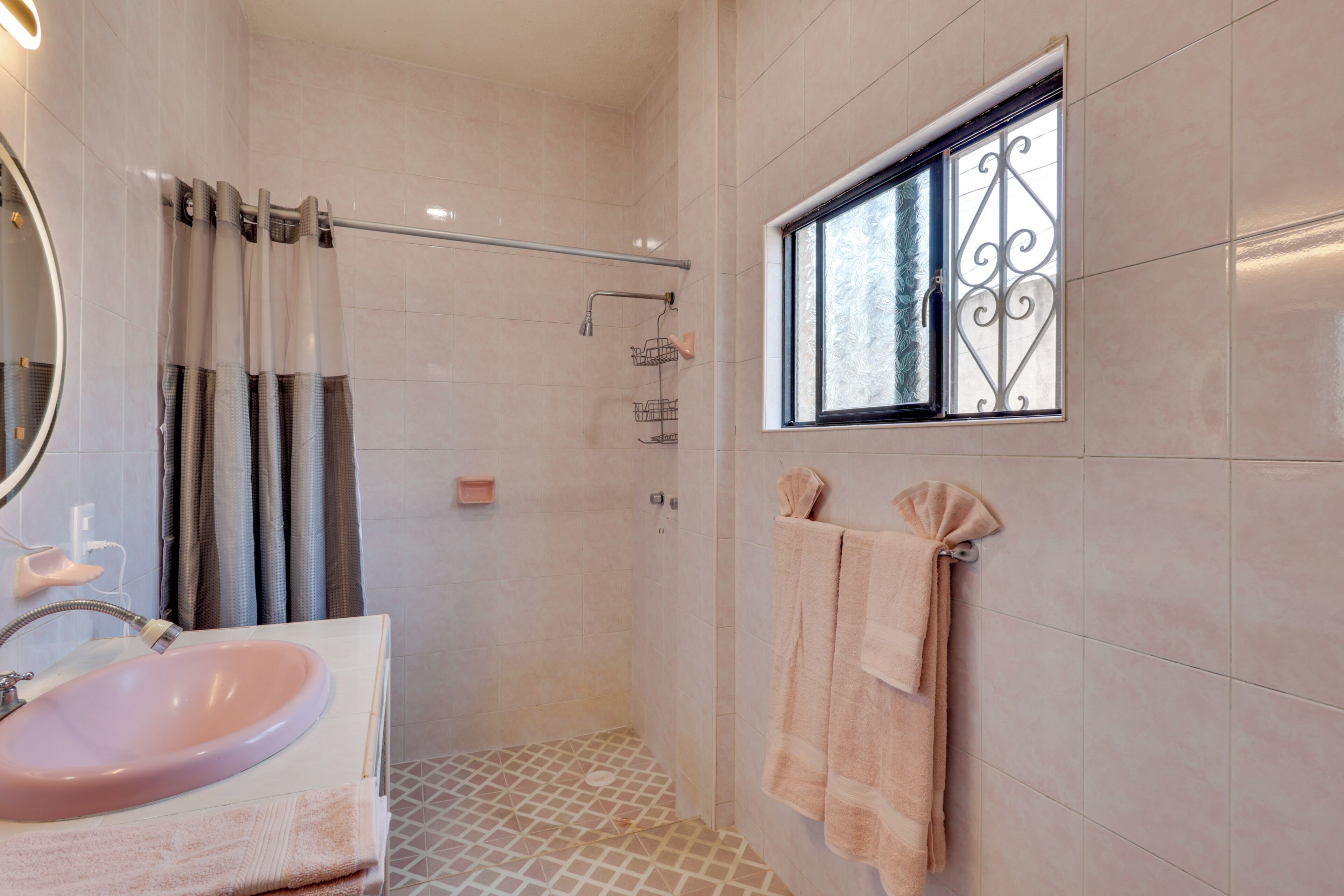 Baño con lavamanos, ducha y ventana con barandales decorativos de hierro.