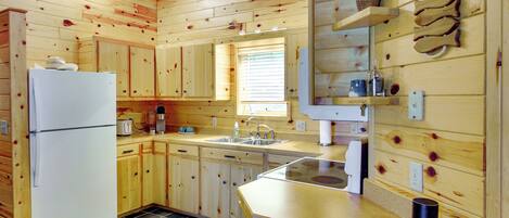 A wooden cabin kitchen with a refrigerator, sink, and wooden cabinets.