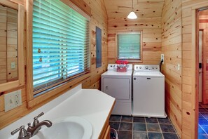 Une petite cabane en bois comprenant une salle de bain équipée d’un lavabo, d’un lave-linge et d’un sèche-linge.